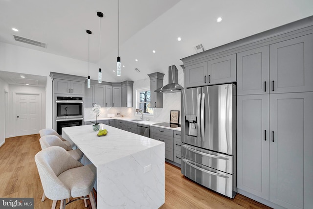 kitchen with gray cabinets, visible vents, appliances with stainless steel finishes, a sink, and wall chimney range hood