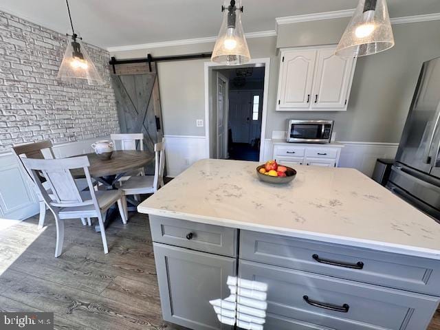 kitchen with a barn door, gray cabinetry, white cabinets, ornamental molding, and stainless steel microwave