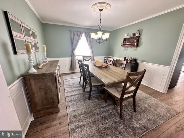 dining room featuring crown molding, wainscoting, wood finished floors, and a notable chandelier