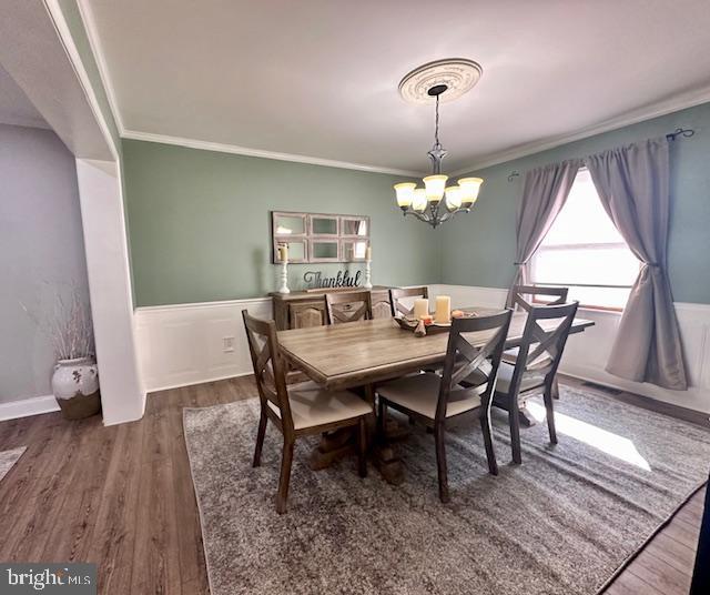 dining area featuring a chandelier, ornamental molding, wainscoting, and wood finished floors