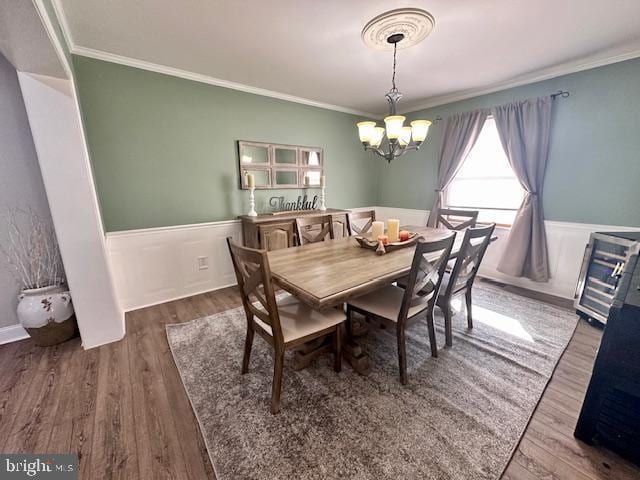 dining space featuring crown molding, a chandelier, wood finished floors, and wainscoting