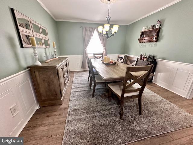 dining area featuring a chandelier, a wainscoted wall, and wood finished floors