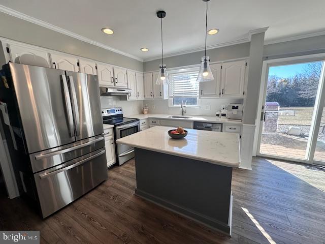 kitchen with under cabinet range hood, stainless steel appliances, white cabinetry, light countertops, and ornamental molding