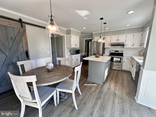 kitchen featuring appliances with stainless steel finishes, wood finished floors, a center island, under cabinet range hood, and white cabinetry