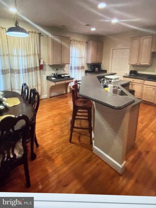 kitchen featuring dark countertops, a sink, a kitchen breakfast bar, and wood finished floors