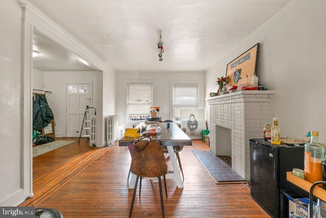 dining room with track lighting, a brick fireplace, wood-type flooring, and radiator heating unit