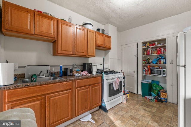 kitchen with white appliances, brown cabinetry, stone finish flooring, a textured ceiling, and a sink