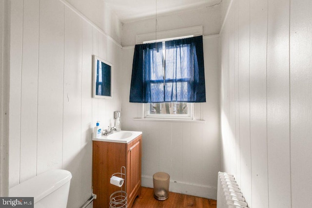 bathroom with toilet, wood finished floors, vanity, and radiator