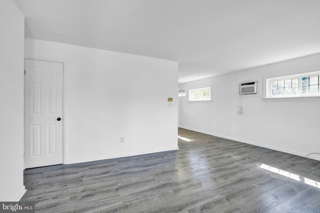 empty room with wood finished floors, a wall unit AC, and baseboards