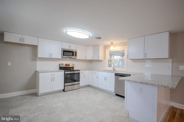 kitchen featuring a peninsula, light stone countertops, stainless steel appliances, white cabinetry, and a sink