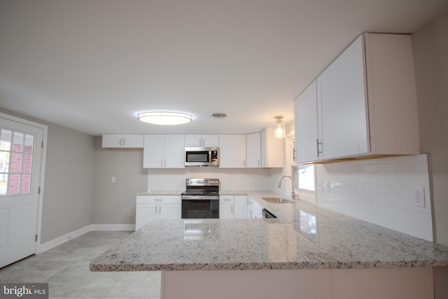 kitchen featuring a peninsula, appliances with stainless steel finishes, light stone counters, and a sink