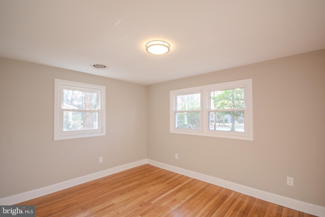 empty room with light wood-style floors, visible vents, and baseboards