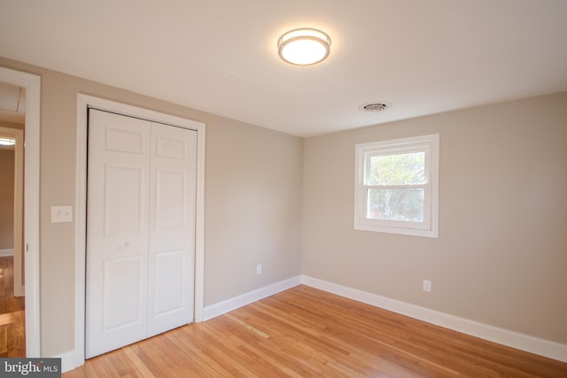 unfurnished bedroom featuring light wood-type flooring, a closet, visible vents, and baseboards