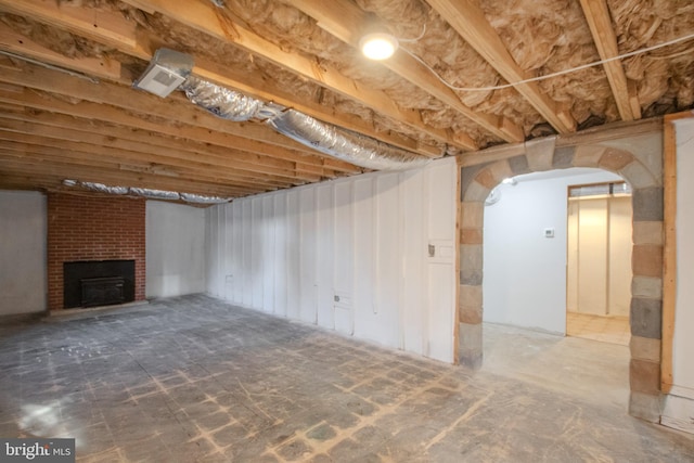 basement with arched walkways and a brick fireplace