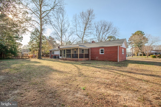 back of property featuring a sunroom, brick siding, a lawn, and a chimney