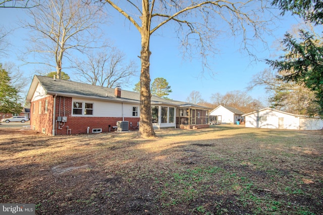 rear view of property with a lawn, a sunroom, a chimney, central air condition unit, and brick siding