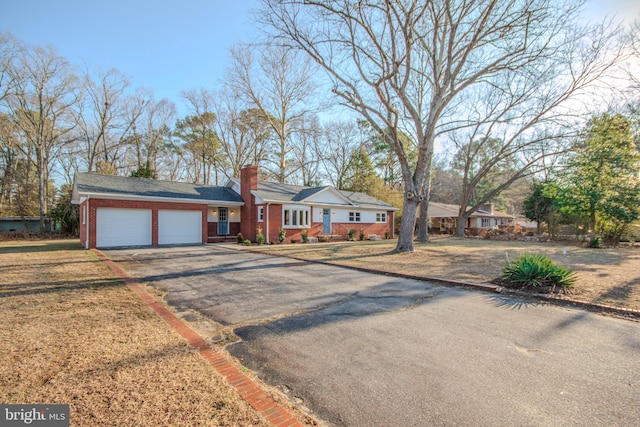 ranch-style house featuring a garage, brick siding, driveway, a chimney, and a front yard