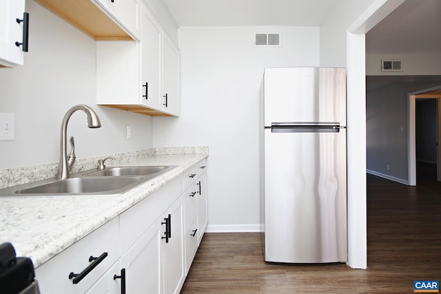 kitchen with visible vents, dark wood-style floors, freestanding refrigerator, white cabinetry, and a sink