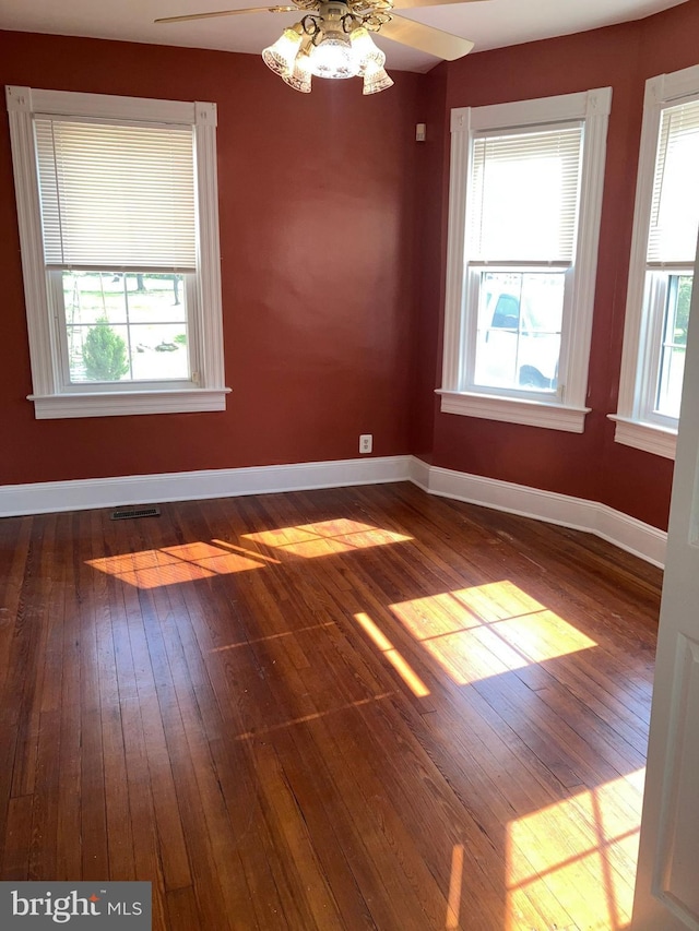 empty room featuring baseboards, dark wood finished floors, visible vents, and a healthy amount of sunlight