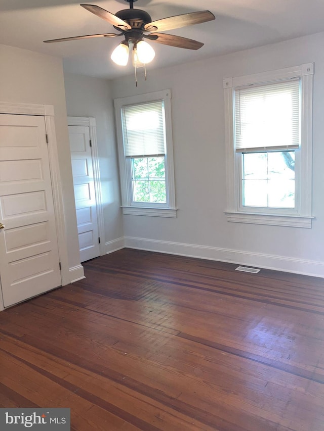 spare room with dark wood-type flooring, visible vents, ceiling fan, and baseboards