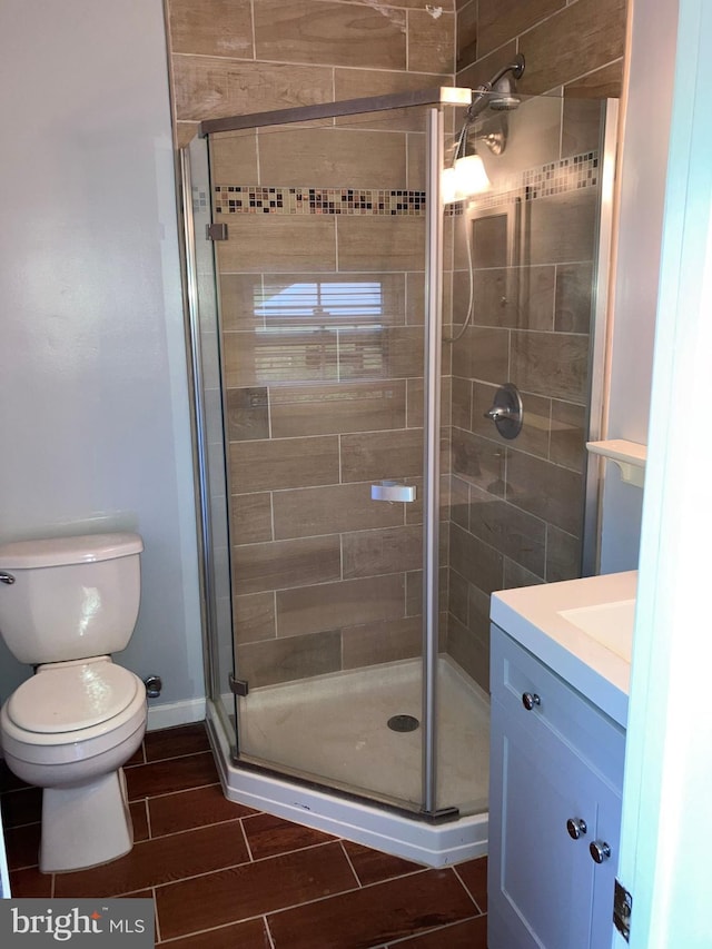 bathroom featuring toilet, vanity, baseboards, wood tiled floor, and a stall shower