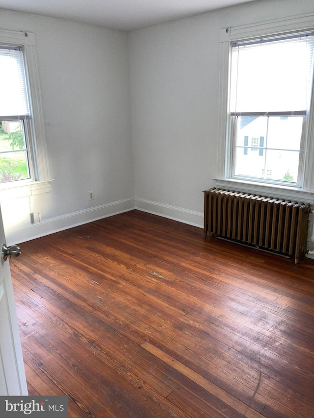 unfurnished room featuring dark wood-type flooring, baseboards, and radiator heating unit