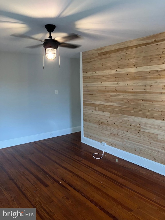 spare room with a ceiling fan, dark wood-style flooring, wooden walls, and baseboards