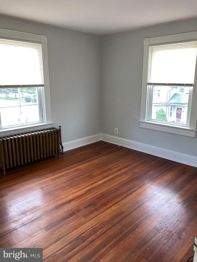 empty room featuring radiator heating unit, baseboards, and dark wood-type flooring