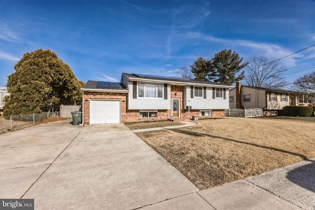 split foyer home with brick siding, an attached garage, roof mounted solar panels, fence, and driveway