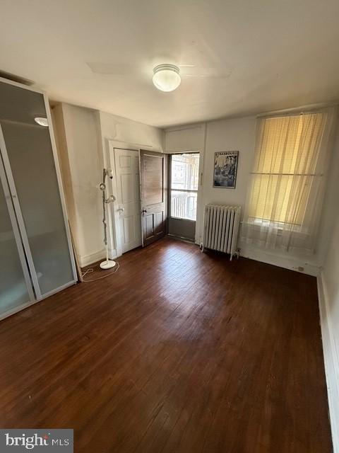 unfurnished bedroom featuring radiator, dark wood-style floors, and baseboards