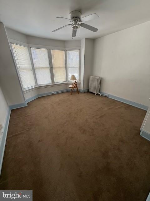 empty room featuring carpet floors, radiator, ceiling fan, and baseboards