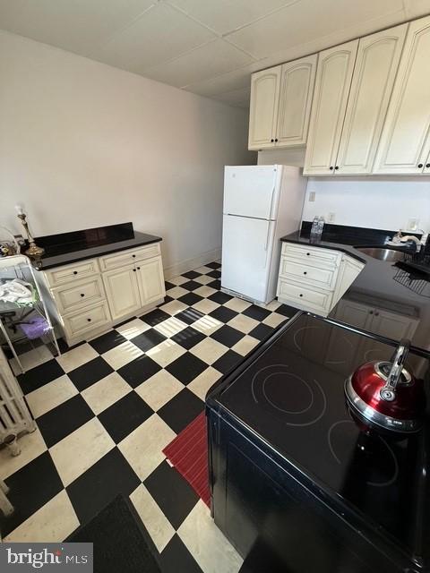 kitchen featuring a sink, black electric range, freestanding refrigerator, light floors, and dark countertops