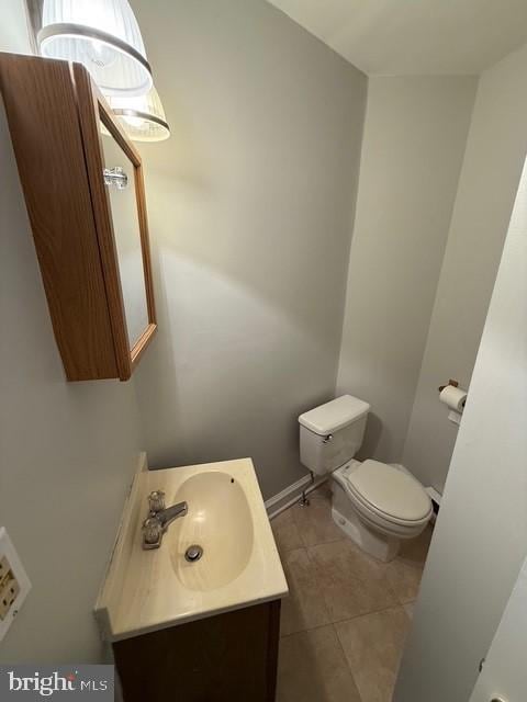 half bath featuring baseboards, vanity, toilet, and tile patterned floors