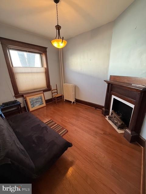 living area with a fireplace with flush hearth, radiator heating unit, wood finished floors, and baseboards