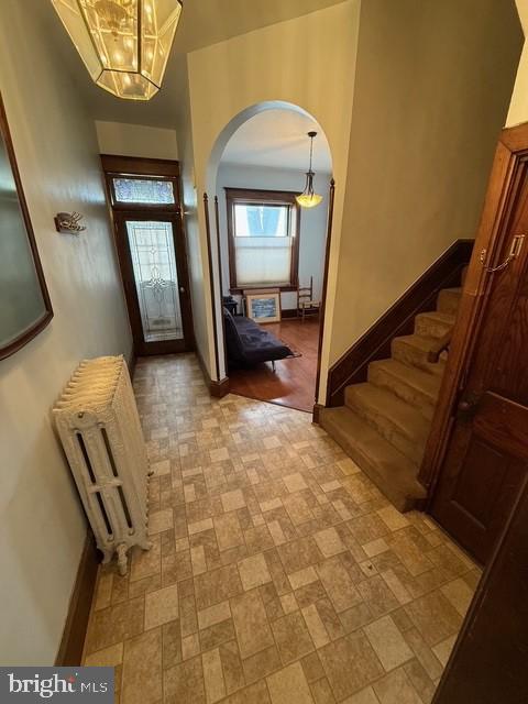 foyer entrance with arched walkways, radiator heating unit, stairs, and baseboards