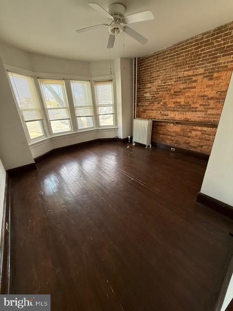 unfurnished living room featuring brick wall, radiator heating unit, baseboards, and dark wood-style flooring