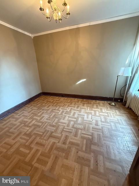 empty room featuring ornamental molding, a notable chandelier, and baseboards