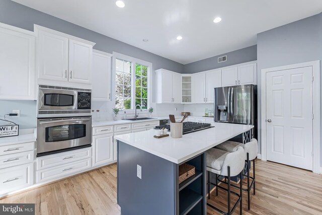 kitchen with a sink, stainless steel appliances, white cabinetry, a kitchen bar, and visible vents