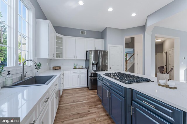 kitchen featuring blue cabinets, a sink, appliances with stainless steel finishes, and white cabinets
