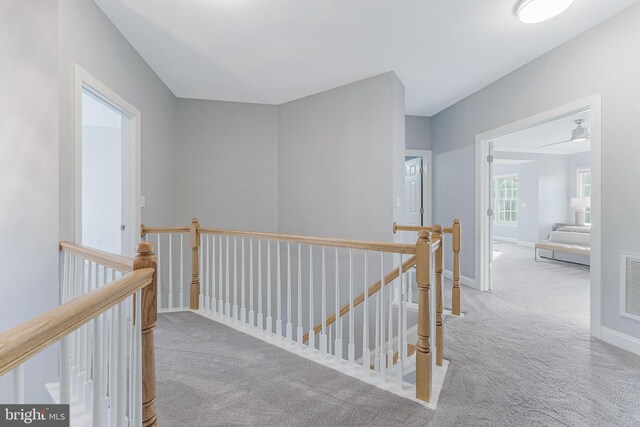 corridor with carpet floors, baseboards, an upstairs landing, and visible vents