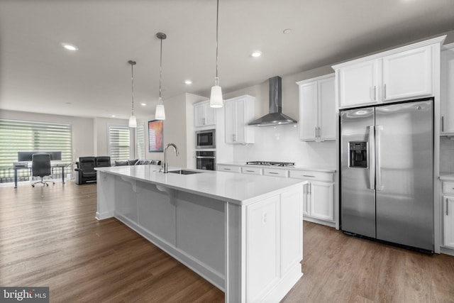 kitchen with light countertops, wood finished floors, stainless steel appliances, wall chimney exhaust hood, and a sink