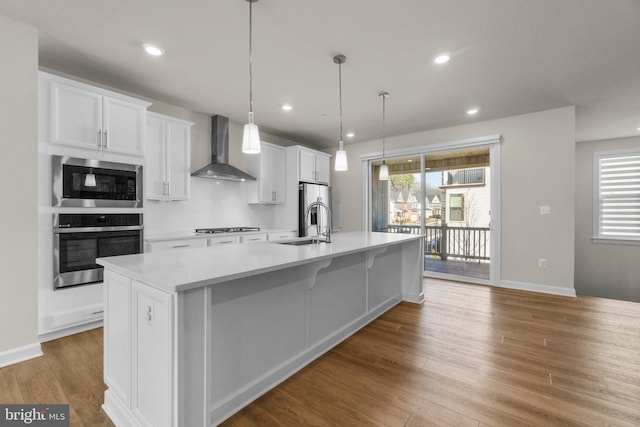 kitchen with a large island, light wood-style flooring, white cabinetry, stainless steel appliances, and wall chimney range hood