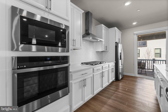 kitchen with light countertops, wall chimney range hood, dark wood-type flooring, and appliances with stainless steel finishes