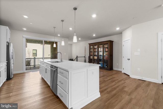 kitchen with a sink, stainless steel appliances, light wood-type flooring, and a kitchen island with sink