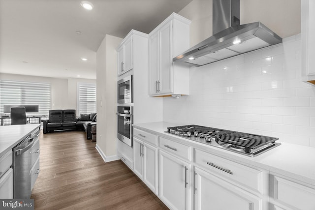 kitchen with wall chimney range hood, dark wood finished floors, light countertops, appliances with stainless steel finishes, and white cabinets