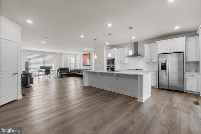 kitchen with stainless steel refrigerator with ice dispenser, a sink, open floor plan, wall chimney exhaust hood, and built in microwave