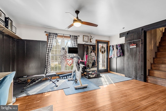 workout room featuring ceiling fan, hardwood / wood-style floors, and a barn door