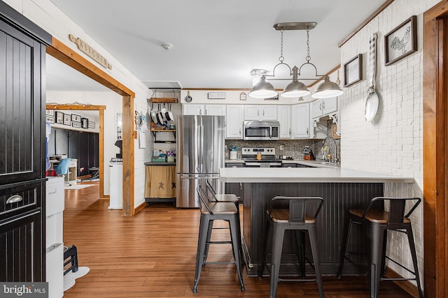 kitchen with a peninsula, a sink, wood finished floors, light countertops, and appliances with stainless steel finishes