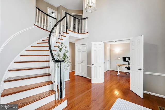 stairway featuring wood-type flooring, a towering ceiling, and baseboards