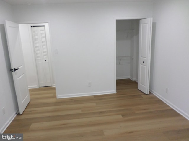 unfurnished bedroom with a spacious closet, a closet, light wood-style flooring, and baseboards